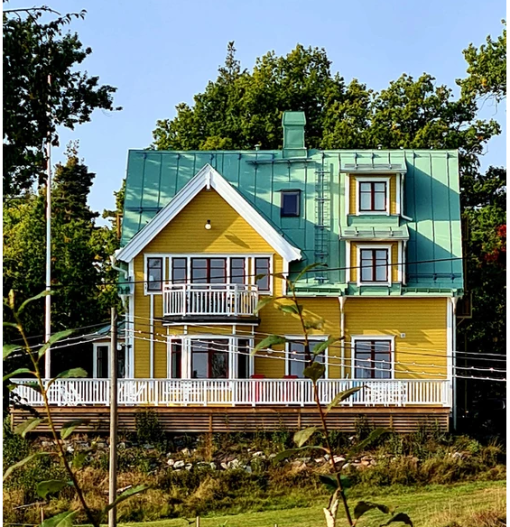 Strömsborgs vilohem gul villa med grönt tak i skogsmiljö med gräsmatta framför.